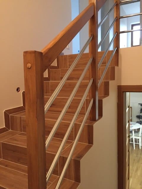 Schody wyłożone brązowymi płytkami z drewnianą poręczą i metalowymi prętami, widok z dołu, naturalne światło.