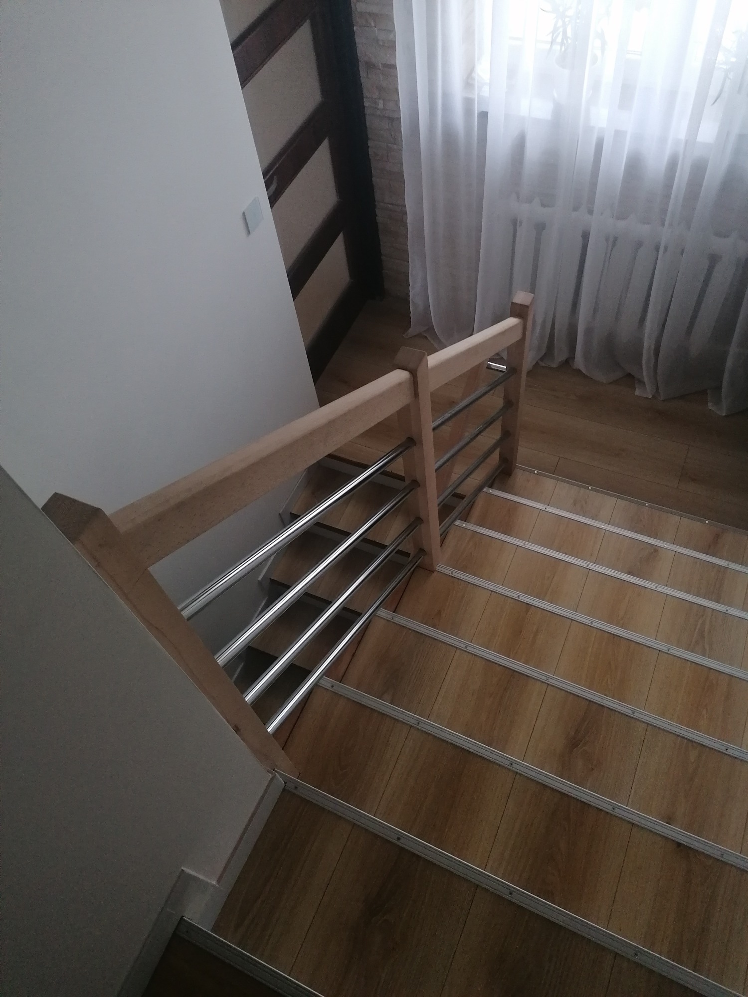 Schody z drewnopodobnymi panelami i jasną, drewnianą poręczą ze stalowymi wypełnieniami, widok z góry.