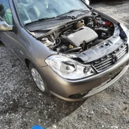 Szary samochód z otwartą maską, widoczny silnik i elementy mechaniczne, zaparkowany na żwirowym podłożu.