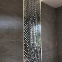 Szara łazienka z akcentem mozaiki lustrzanej podświetlonej ledami, tworząca pionowy pas dekoracyjny.