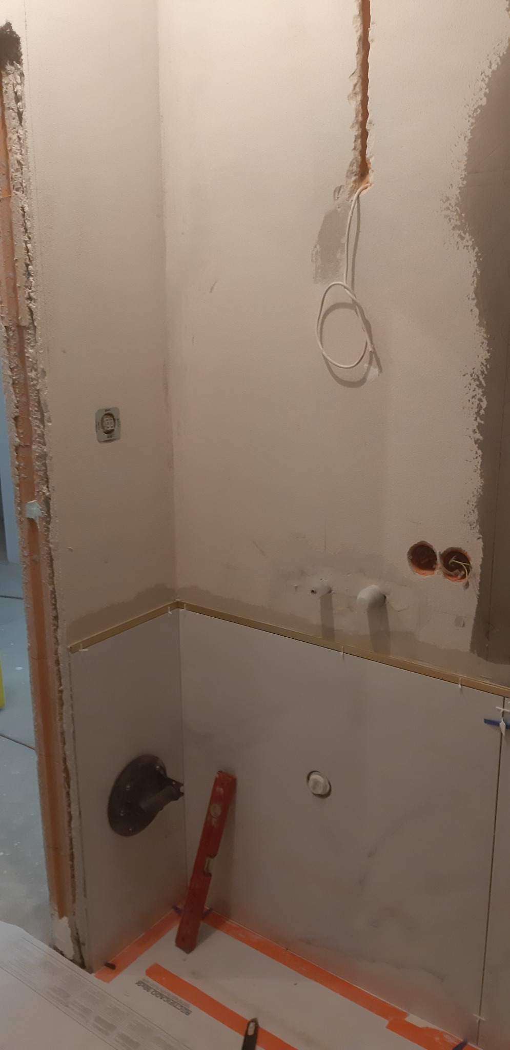 Fragment łazienki w trakcie prac wykończeniowych: częściowo wyłożone płytki, widoczne przewody elektryczne, poziomica oparta o ścianę, listwa przypodłogowa oraz elementy instalacji wodnej.