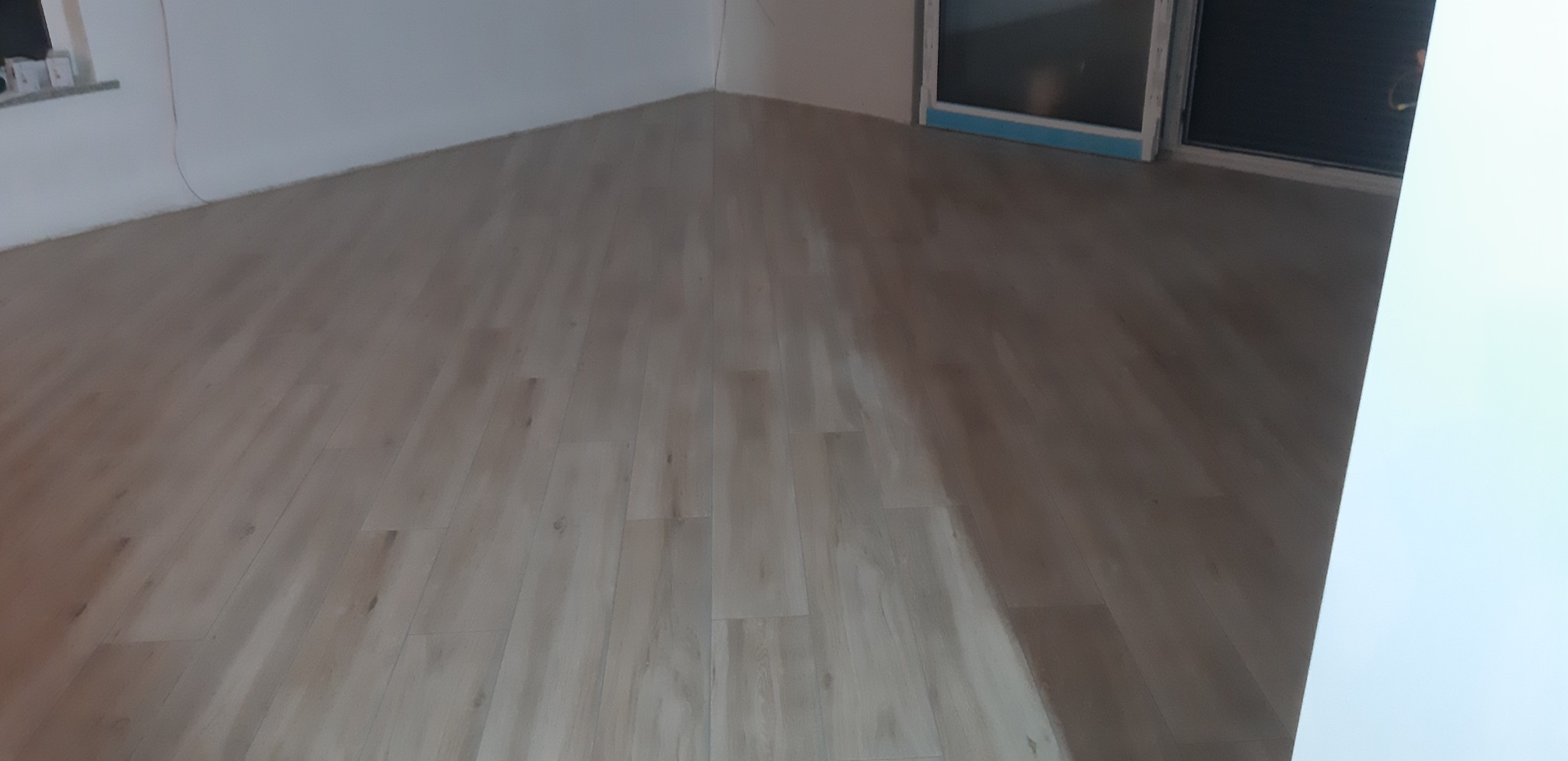 Jasne panele podłogowe ułożone w nowym, jeszcze pustym pomieszczeniu, widok z góry na świeżo wykończoną podłogę, ściany pomalowane na biało.