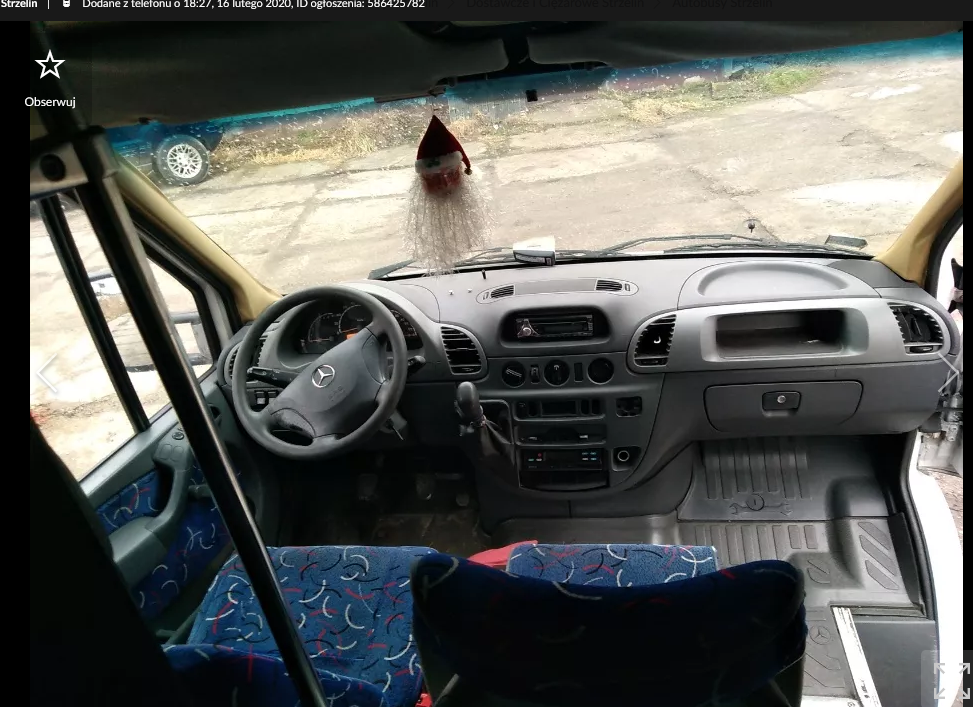 Wnętrze kabiny busa marki Mercedes z widocznym kokpitem, kierownicą z logo Mercedesa, fotelami z niebieską tapicerką w biało-czerwone wzory oraz zawieszką w kształcie Mikołaja pod przednią szybą.