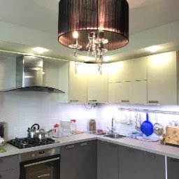 Nowoczesna kuchnia z szarymi szafkami, białymi płytkami na ścianie i dekoracyjnym żyrandolem z czarnym abażurem i kryształkami.