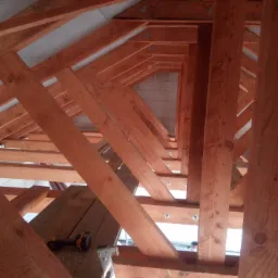 Konstrukcja drewniana dachu z widoczną wiertarką na rusztowaniu w Jaworzynce, ukazująca etap budowy domu.