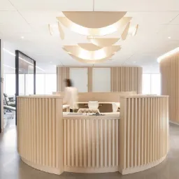 Jasna recepcja biurowa z drewnianymi panelami i designerską lampą sufitową, widok na przeszklone biuro w tle.