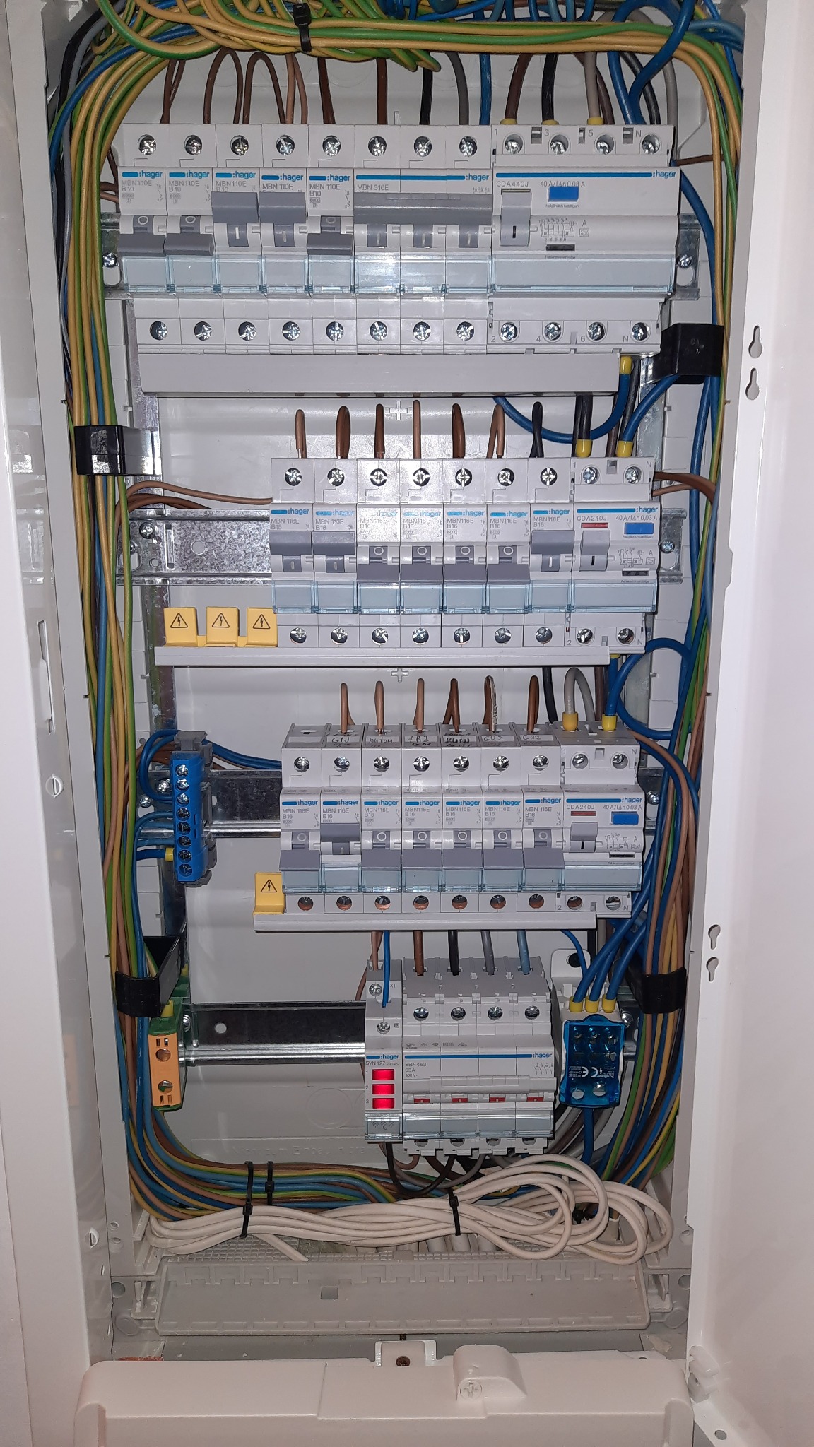 Rozdzielnica elektryczna Hager z zainstalowanymi bezpiecznikami i przewodami w różnych kolorach, widok z bliska na wnętrze szafki.