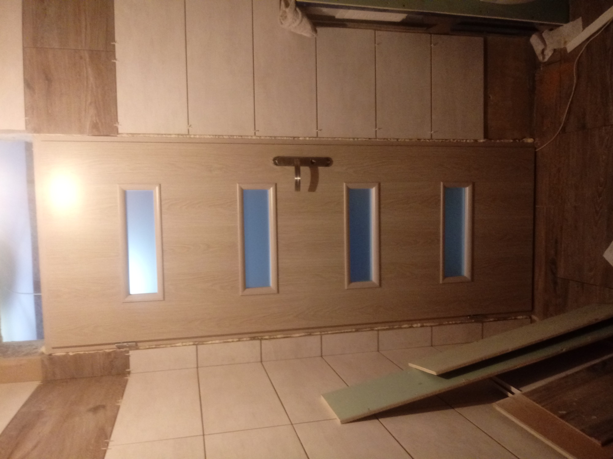 Dębowa, wewnętrzna ościeżnica z czterema prostokątnymi przeszkleniami, zamontowana w trakcie wykańczania wnętrza, widoczne płytki ceramiczne na ścianach i podłodze, oraz deski podłogowe w rogu...