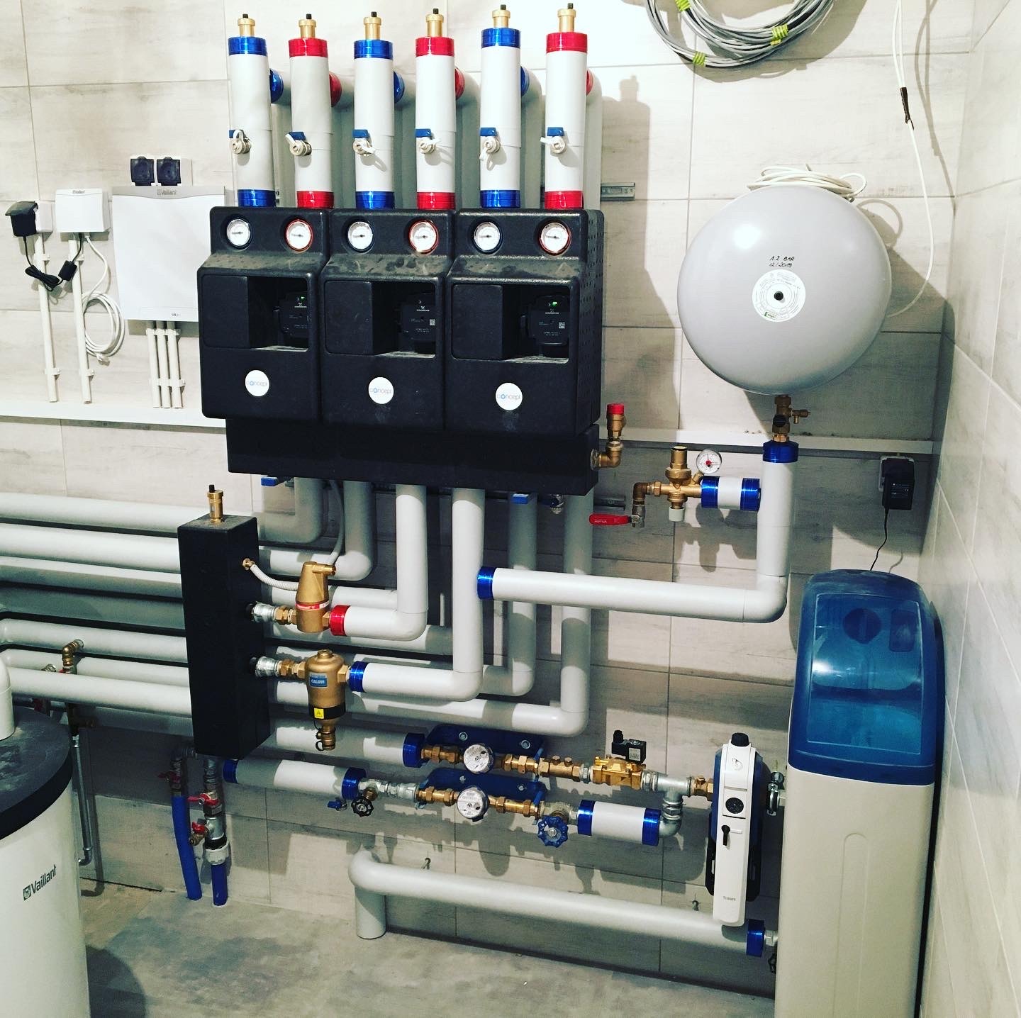 Rozbudowana instalacja grzewcza z rozdzielaczem, pompami obiegowymi, naczyniem wzbiorczym i zmiękczaczem wody w kotłowni wykończonej płytkami ceramicznymi.
