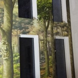 Der-bud - Ściana z fototapetą leśną i czterema oknami z białymi ramami. Na pierwszym planie narzędzie. Drzewo z wyciętą twarzą dodaje unikalnego charakteru.