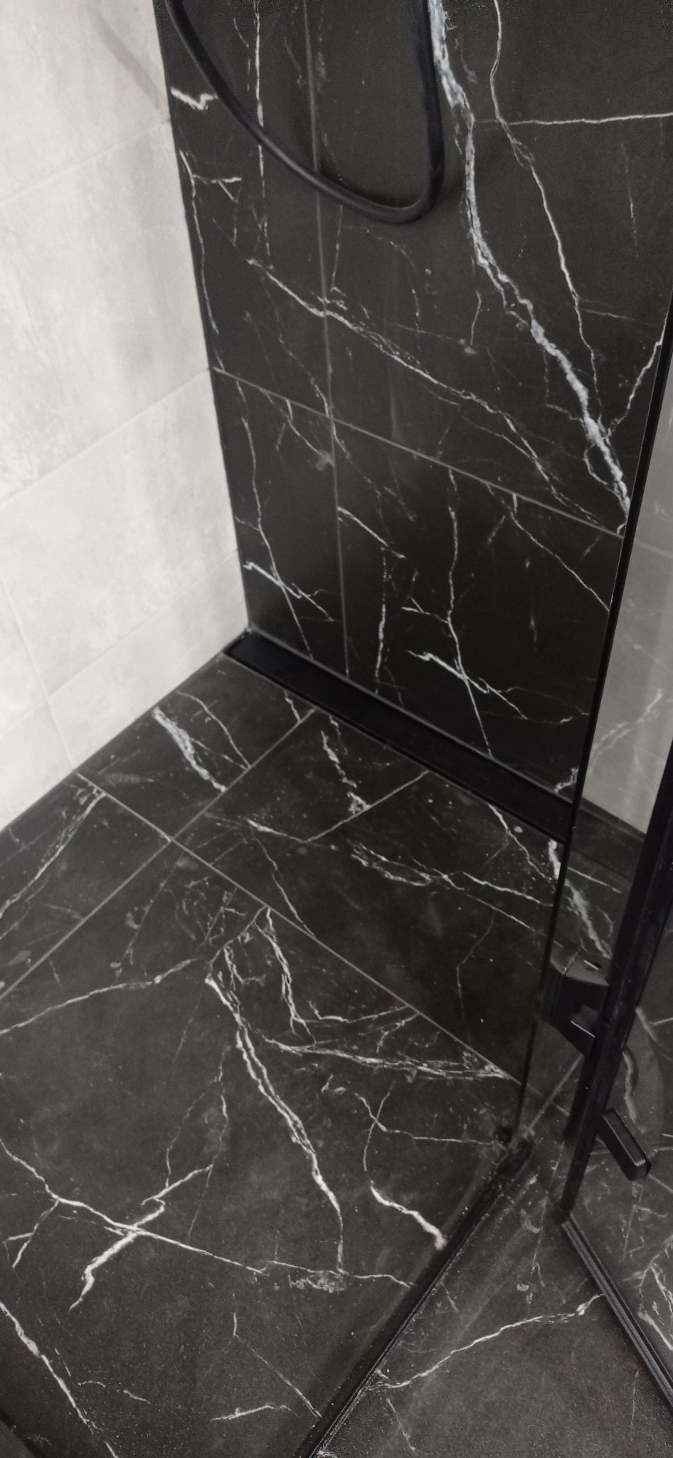 Kabina prysznicowa z czarnych płytek imitujących marmur, z odpływem liniowym i fragmentem szklanej ściany.