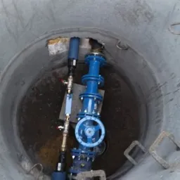 Niebieska armatura wodna z zaworem motylkowym i filtrami wewnątrz betonowej studni kanalizacyjnej w Mysłowicach, widok z góry.