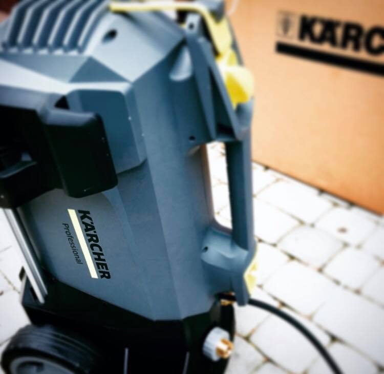 Profesjonalna myjka ciśnieniowa Karcher Professional na kostce brukowej, z pudełkiem Karcher w tle, gotowa do użycia.
