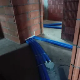 Niebieskie rury poprowadzone w nowym budynku w trakcie budowy, widoczne ceglane ściany w surowym stanie.