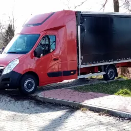 Czerwony bus dostawczy z czarną plandeką na parkingu z kostki brukowej, widoczna tablica rejestracyjna i logo Lamico.