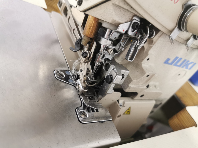 Detale przemysłowej owerlok maszyny szwalniczej marki JUKI, widoczne igły, stopka i elementy mechaniczne.
