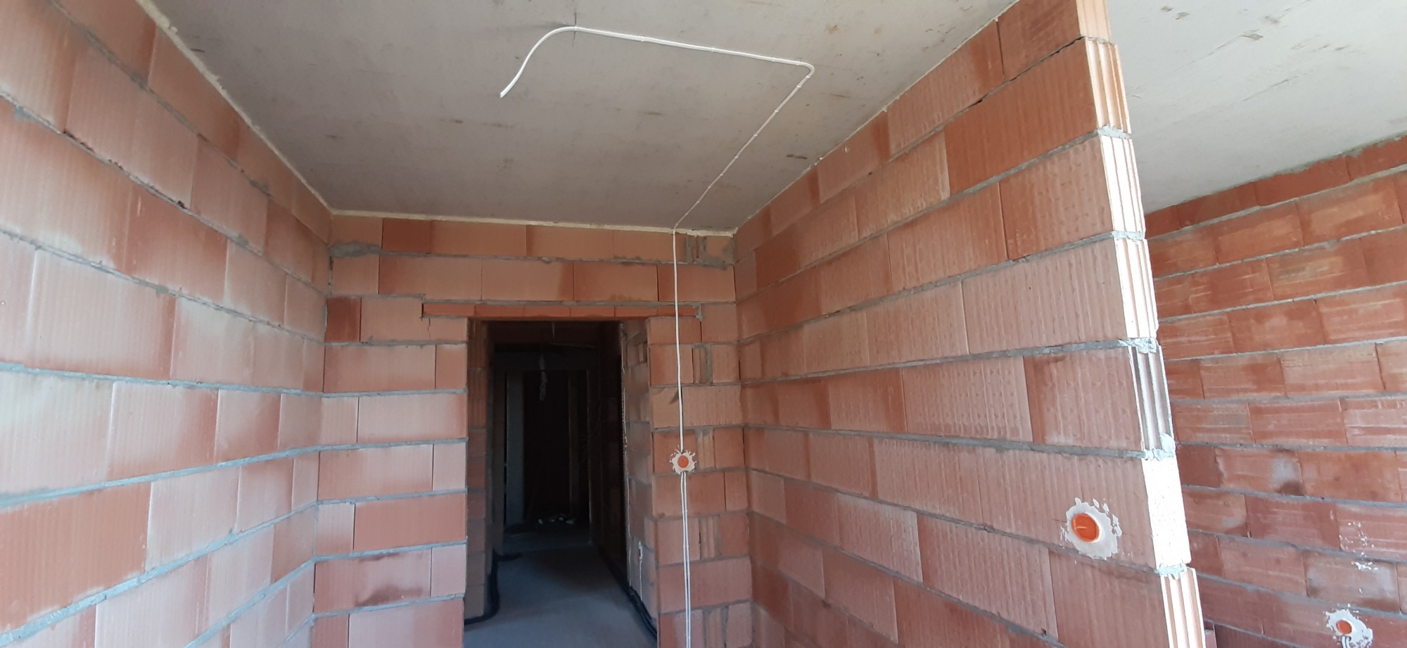 Surowy stan wnętrza z czerwonej cegły z widoczną instalacją elektryczną: kable prowadzone po suficie i ścianach, puszki elektryczne osadzone w murze.