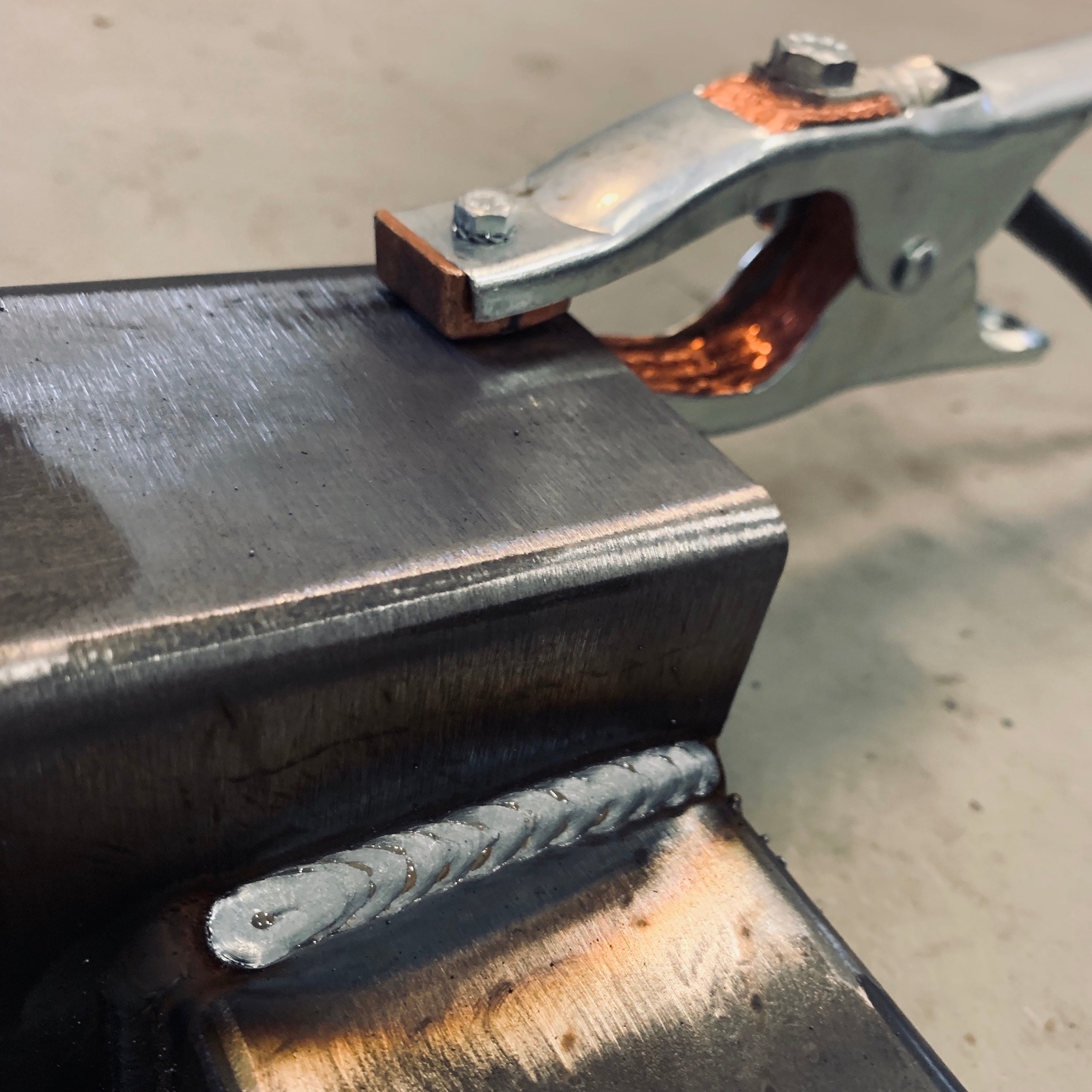 Spoina na profilu stalowym, uchwyt spawalniczy przymocowany do elementu, widoczne ślady po spawaniu.