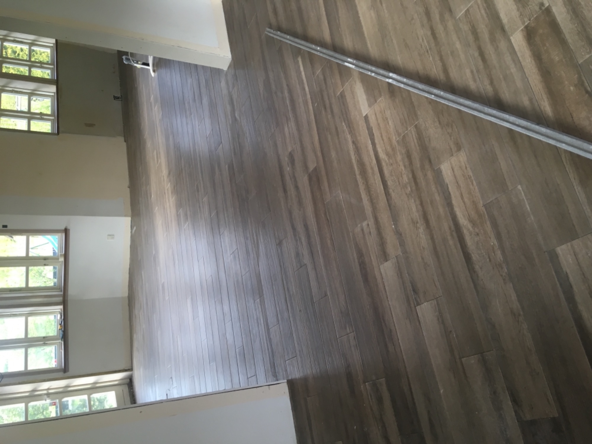 Ułożona podłoga z paneli imitujących drewno, widoczne okna i listwa przypodłogowa w trakcie montażu, wnętrze w trakcie wykańczania.