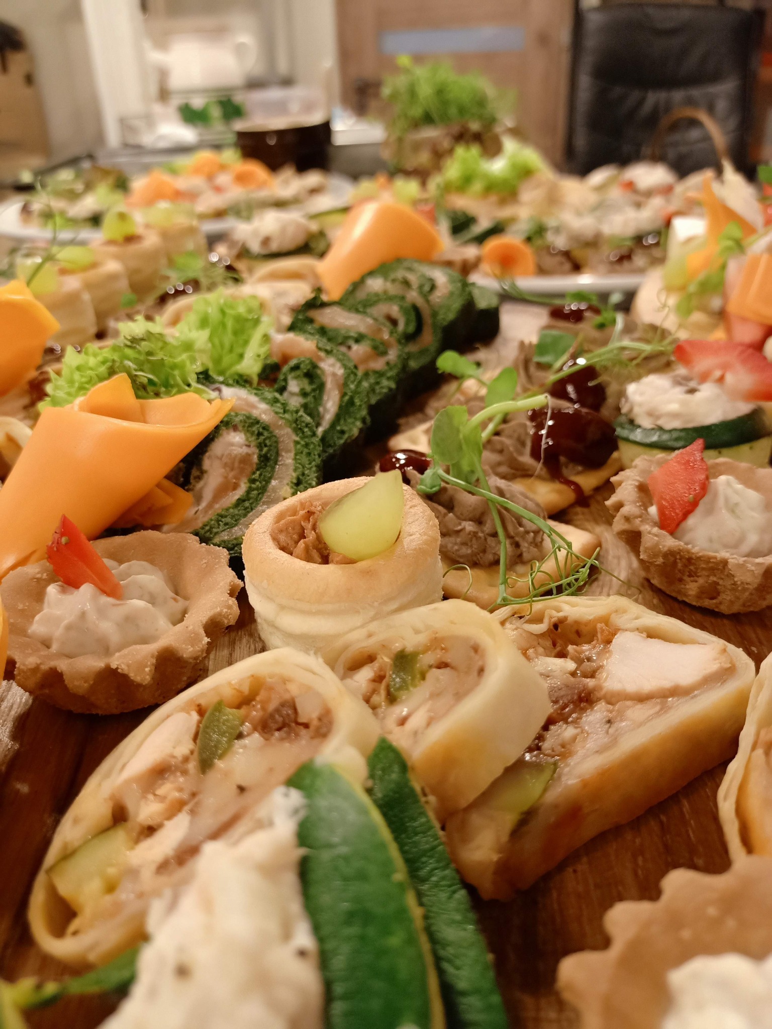 Bogaty wybór przekąsek na drewnianej desce: roladki z zielonym szpinakiem, tartaletki z kremowym nadzieniem i papryką, vol-au-venty z farszem, roladki z kurczakiem i warzywami, całość udekorowana...