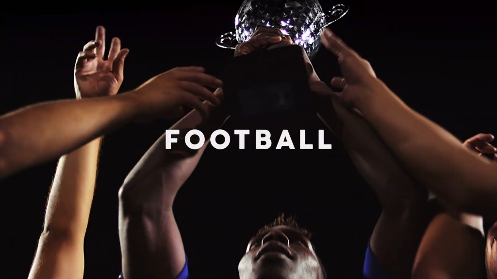 Ujęcie od dołu: Ręce unoszą błyszczący puchar nad głową, ciemne tło, widoczna twarz osoby w dolnej części kadru.