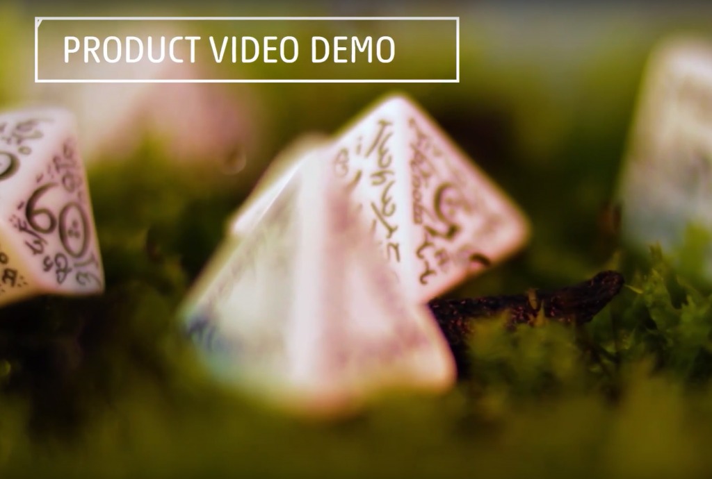 Trzy białe, wielościenne kości do gry z wygrawerowanymi znakami, leżące na mchu, z napisem 'PRODUCT VIDEO DEMO' u góry.