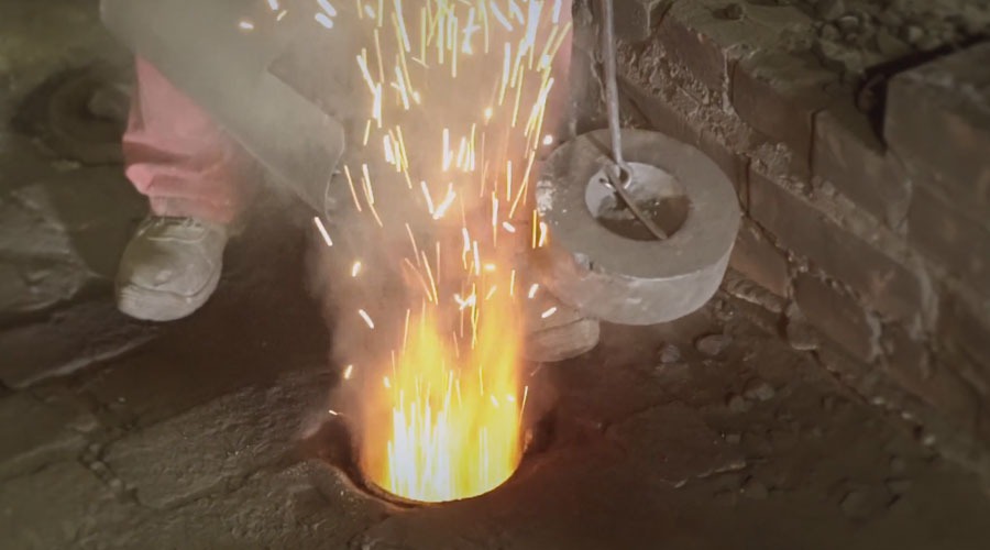 Proces odlewania metalu w Poznaniu, z widocznymi iskrami i dymem wydobywającymi się z formy, obok której stoi pracownik w roboczym ubraniu.
