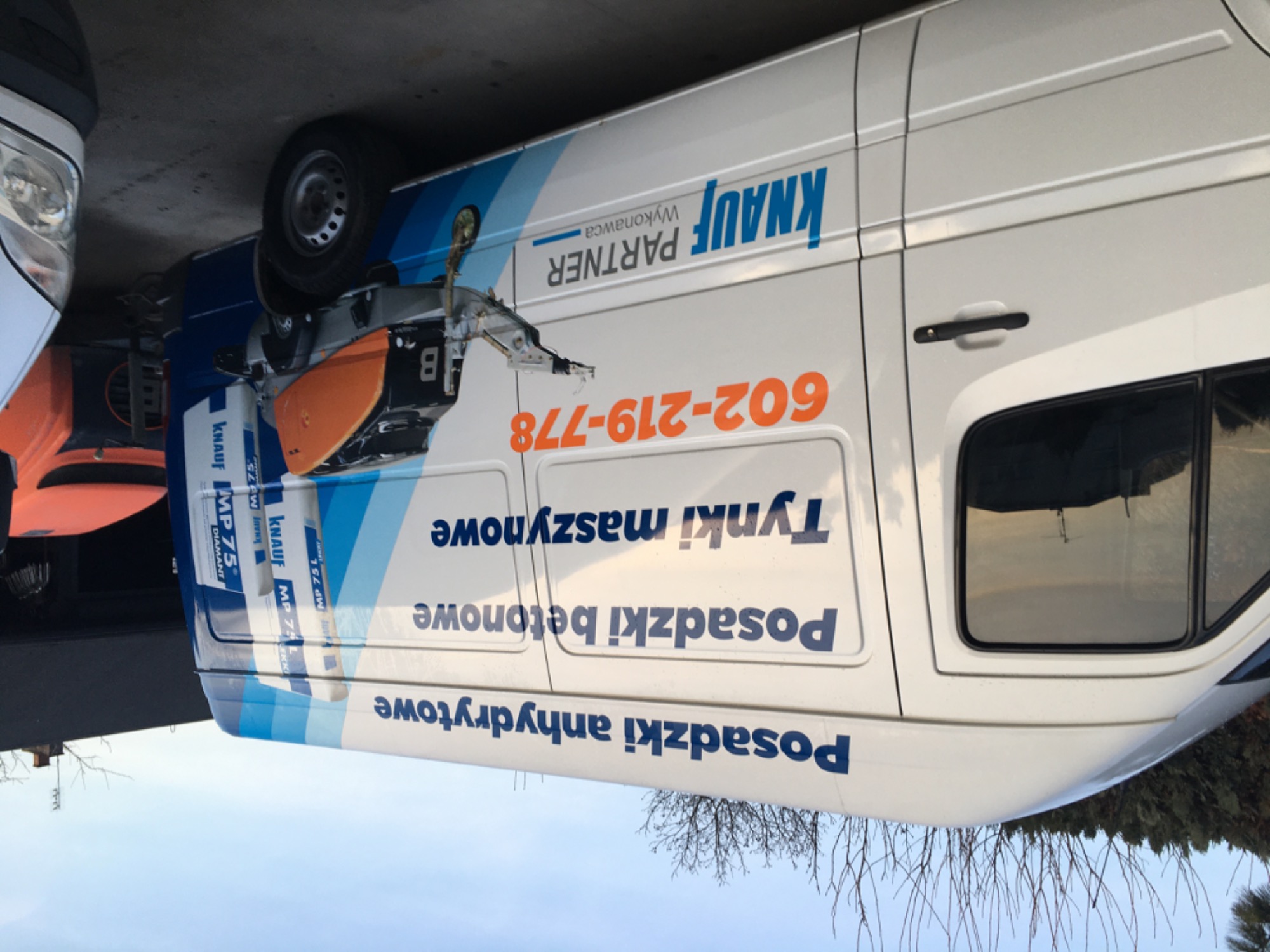 Biały samochód dostawczy z reklamą firmy Knauf Partner Wykonawca, oferującej posadzki anhydrytowe, betonowe i tynki maszynowe, z numerem telefonu 602-219-778.