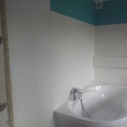 Konbud - Biała wanna narożna w trakcie remontu łazienki, widoczna surowa ściana przed wykończeniem, turkusowy sufit, białe płytki na ścianach.