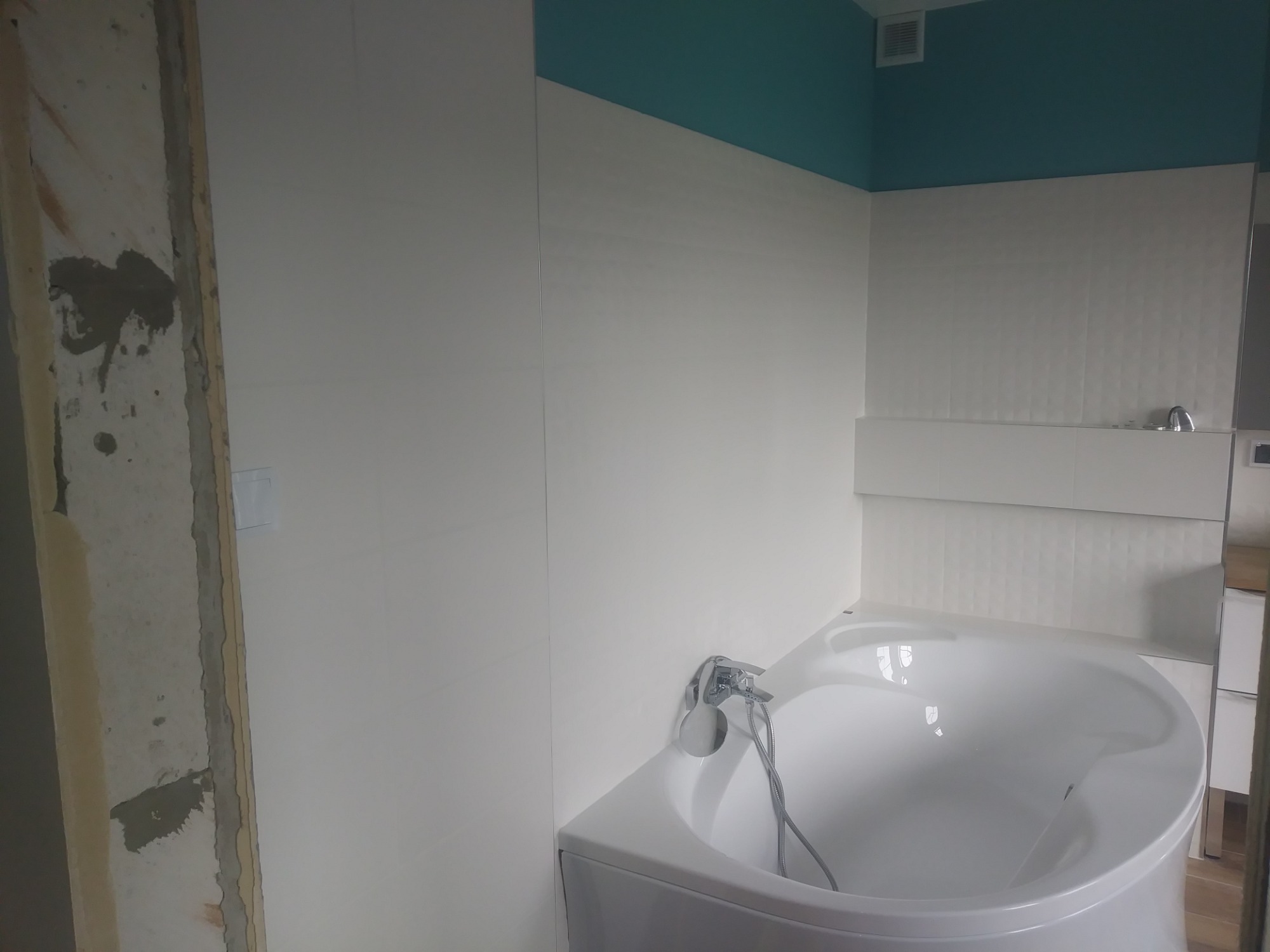 Biała wanna narożna w trakcie remontu łazienki, widoczna surowa ściana przed wykończeniem, turkusowy sufit, białe płytki na ścianach.