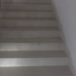 Widok z dołu na wyłożone płytkami schody z drewnianą balustradą, oświetlone z góry, z widoczną fakturą płytek.