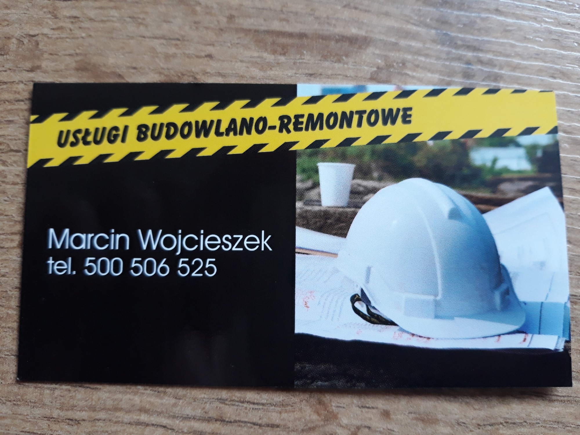 Wizytówka firmy budowlano-remontowej Marcina Wojcieszek z numerem telefonu, z grafiką przedstawiającą biały kask budowlany, kubek i plany na tle zieleni.