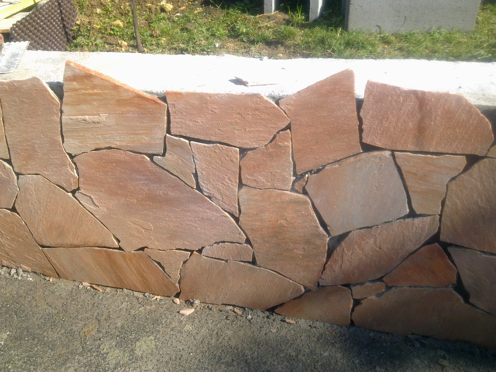 Mur z nieregularnych, płaskich kamieni w odcieniach brązu i beżu, tworzących dekoracyjną ścianę na zewnątrz.