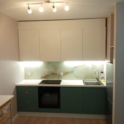 RJA Building - Nowoczesna kuchnia z zielonymi szafkami, białym blatem i marmurowym panelem nad blatem, oświetlona lampami sufitowymi i listwą LED pod szafkami wiszącymi.