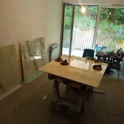 Przygotowanie do układania płytek wielkoformatowych: płyta na kozłach, przyssawki do przenoszenia, plan układania, widok na balkon z zielenią.