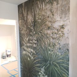 RJA Building - Ściana z fototapetą w tropikalne rośliny, widok z boku, podłoga zabezpieczona folią i taśmą malarską, w tle widoczne puszki z farbami.