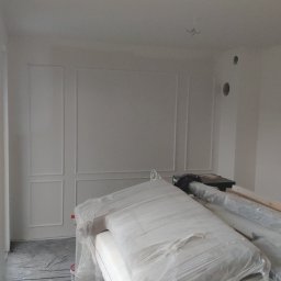 RJA Building - Pokój w trakcie malowania na biało, zabezpieczone meble folią, widoczne listwy dekoracyjne na ścianach.