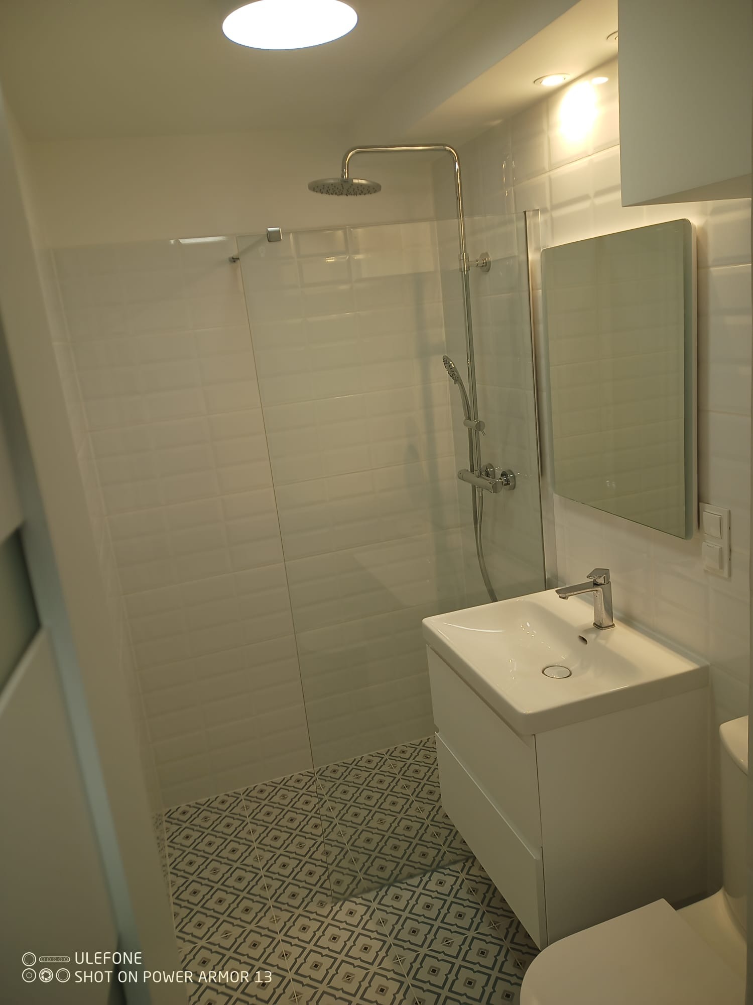 Biała łazienka z kabiną prysznicową typu walk-in, umywalką z szafką i wzorzystą podłogą. Realizacja wykończenia łazienki w Gdańsku.