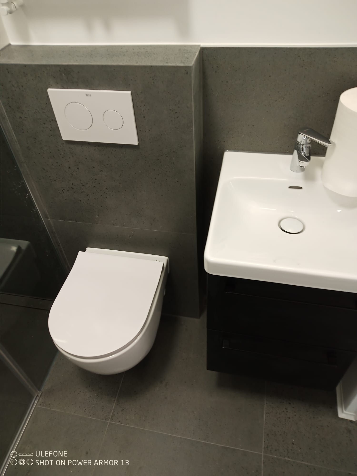 Nowoczesna łazienka z podwieszaną toaletą Roca, umywalką nablatową i szarą okładziną ścienną. Minimalistyczny design.