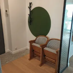 Dwa drewniane fotele kinowe z tapicerką w pepitkę stoją na parkiecie, na ścianie zielone koło i czarny wieszak w kształcie drzewa.