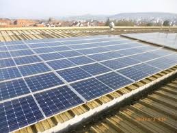 Rząd paneli słonecznych na dachu budynku, widok z góry, z rozmytym tłem miejskim.