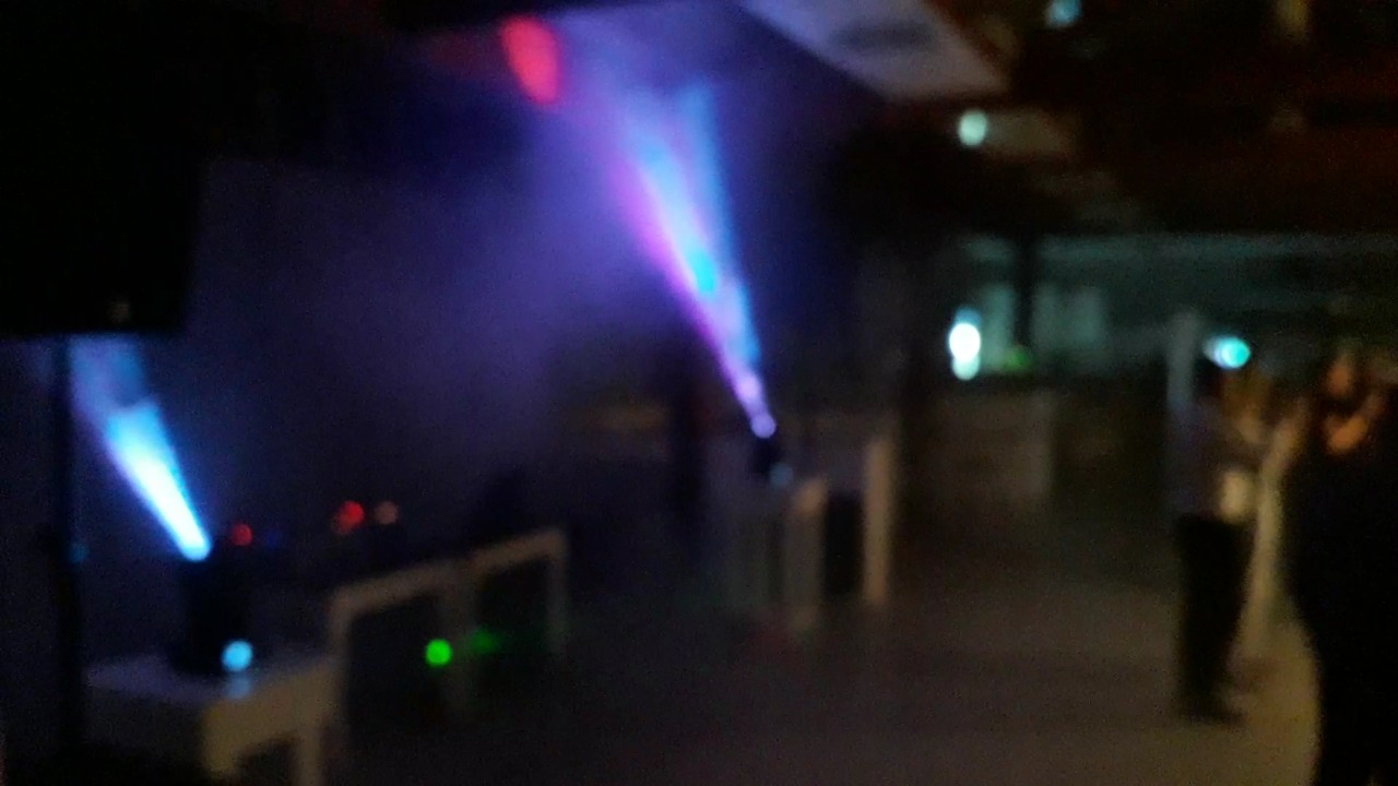 Efekty świetlne: niebieskie i fioletowe promienie reflektorów oświetlają ciemne wnętrze, widoczne osoby w tle.