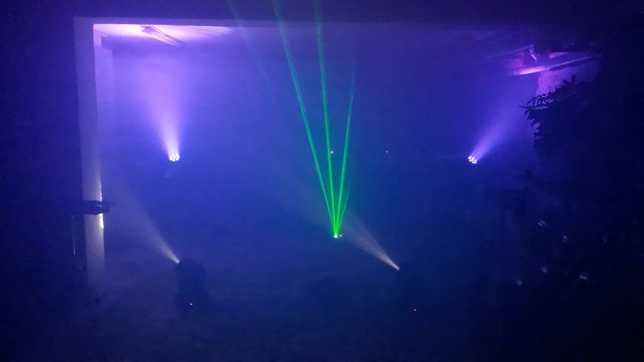 Scena oświetlona reflektorami LED w kolorze fioletowym i zielonym, z efektem lasera i mgły, wewnątrz prawdopodobnie betonowego budynku.