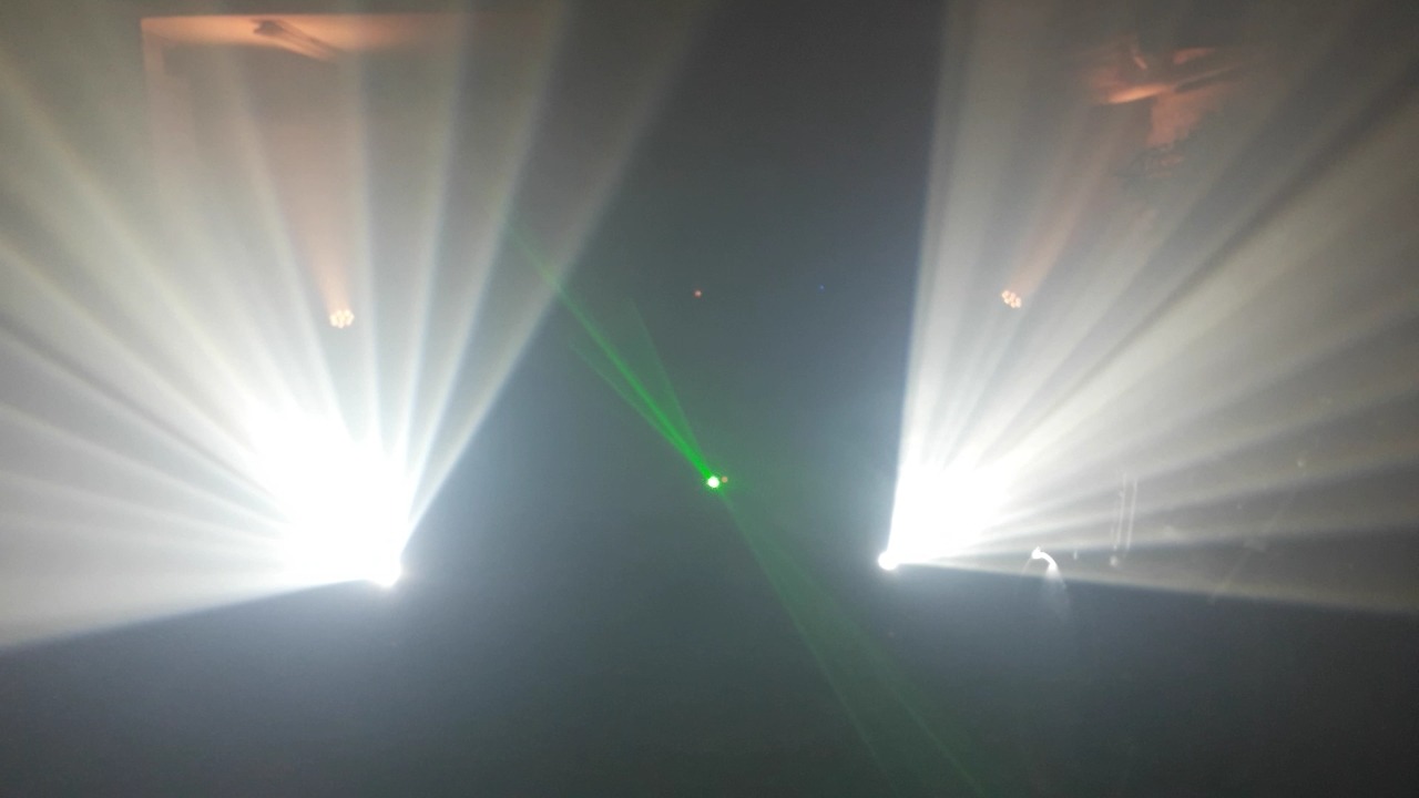 Scena w ciemności oświetlona dwoma reflektorami z promieniami światła oraz zielonym laserem.