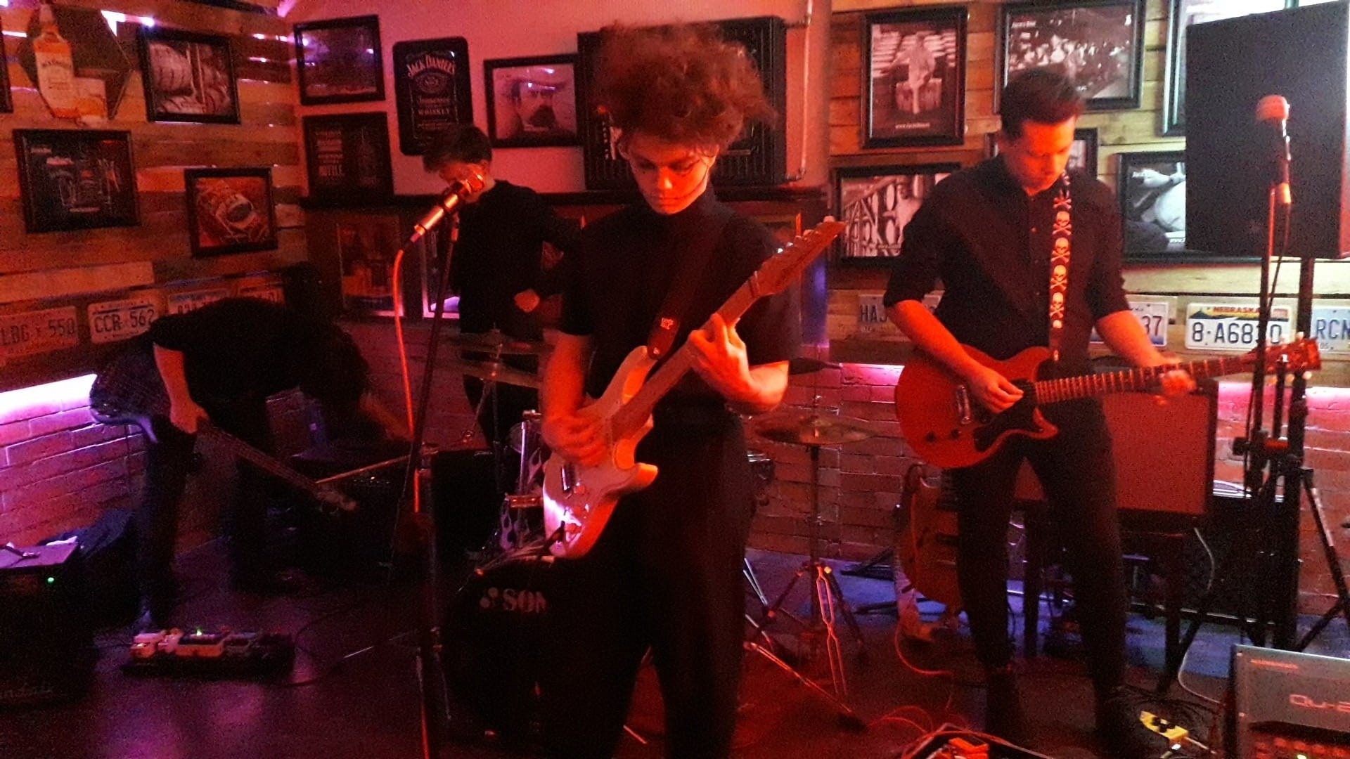 Zespół muzyczny grający koncert w barze z dekoracjami w stylu vintage, oświetlenie sceniczne w odcieniach czerwieni i fioletu.