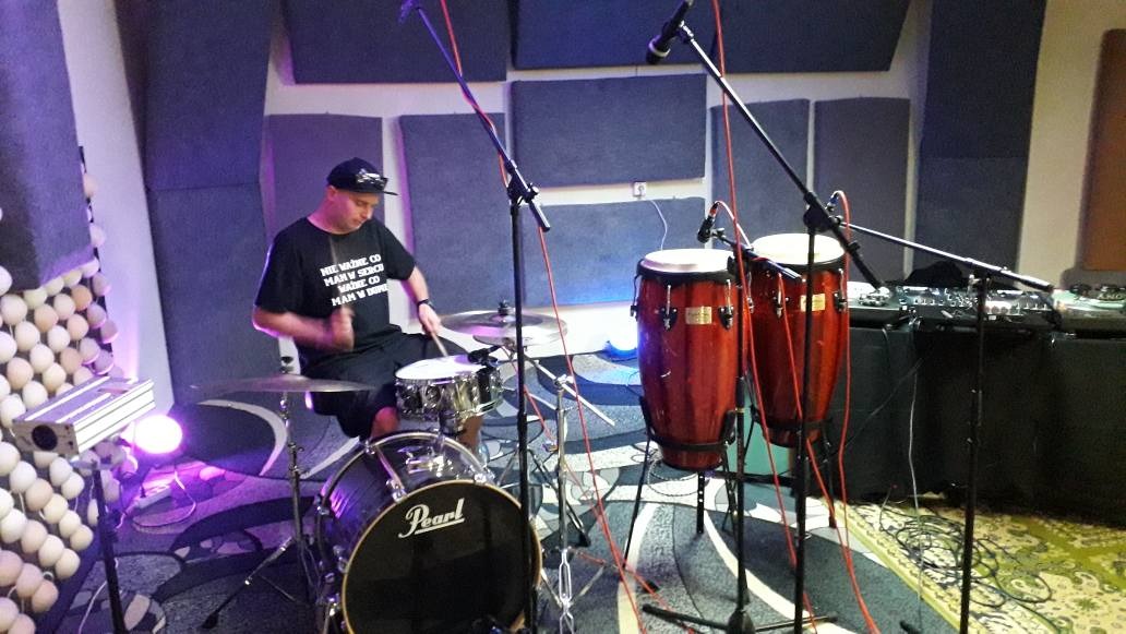 Perkusista gra na perkusji i bębnach conga w studiu nagraniowym z panelami akustycznymi i mikrofonami