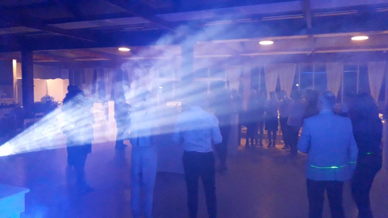 Oświetlenie sceniczne tworzące efekt mgły i promieni podczas imprezy, widoczni ludzie w tle i na pierwszym planie.