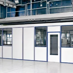 Białe kontenery biurowe z niebieskimi ramami okiennymi i drzwiowymi w przestrzeni magazynowej, z widocznymi instalacjami wentylacyjnymi pod sufitem.