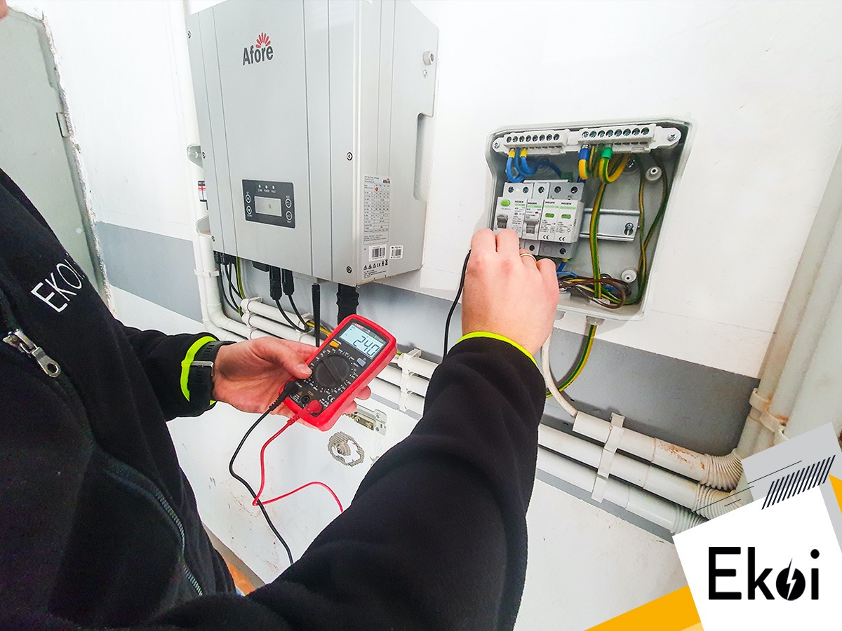 Elektryk mierzy napięcie w skrzynce rozdzielczej obok falownika Afore za pomocą multimetru z czerwonym wyświetlaczem.