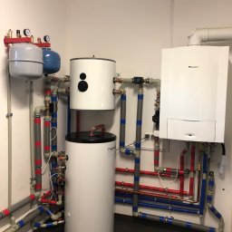 Przyjazna Energia.com. Sp.z o.o. - Kompletna instalacja kotłowni z zasobnikiem ciepłej wody, zbiornikami wyrównawczymi, pompą obiegową i kotłem gazowym Junkers, widoczne liczne rury w izolacji z oznaczeniami kolorystycznymi.